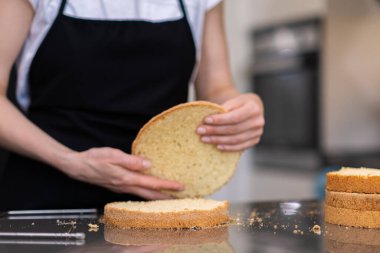 Modern mutfaktaki glütensiz yemek pişirme sürecinden hazırlanmış kesilmiş pasta katmanlarını birbirine bağlayan siyah önlüklü profesyonel şekerleme.