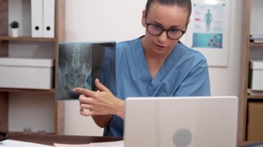 Sanal Radyoloji Danışmanlığı: Doktor bir video görüşmesi yapıyor, bir dizüstü bilgisayarda röntgen filmleri gösteriyor ve teletıp alanındaki hastalara özgü hastalıkların özelliklerini anlatıyor.