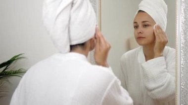 Banyodaki bir kadın, aynanın yanındaki pamukla cildini temizler. Güzellik ve özgüven saçar.. 