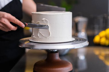 Becerikli bir pastacı, arka planda bulanık bıçaklı beyaz mastikte geleneksel düğün kutlaması için ev yapımı pasta hazırlıyor.