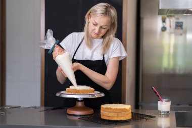 Pasta külahını kullanarak mutfak masasında duran sarışın ev hanımına lezzetli organik krema sürerek ev yapımı özel şekerlemeler yapmaya odaklanmış.
