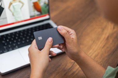 Dişi eller, internetten giysi mağazası ödemelerinin internet üzerinden yapıldığı bir web sitesi olan dizüstü bilgisayara karşı temas kurulamayan e-ödemeler için çipli koyu renk bir kredi kartı tutuyor.