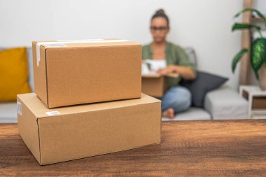 Arka planda bir kadın çevrimiçi alışveriş paketleri, nakliye ve pazar alışveriş kavramlarını taşırken boş paket kutuları masanın üzerinde duruyor.. 