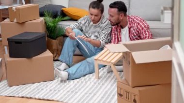 Neşeli genç bir çift, modern ahşap raf mobilyalarını taşınan kutuların arasında birleştiriyor ve yeni dairelerini DIY ev dekorasyonuyla donatıyorlar.