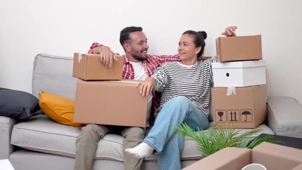 ホーム スウィートホーム 幸せな若い結婚したカップルは ソファにリラックス 多数のボール紙箱に囲まれて うまく新しいアパートに移動した後 まだ疲れています — ストック動画