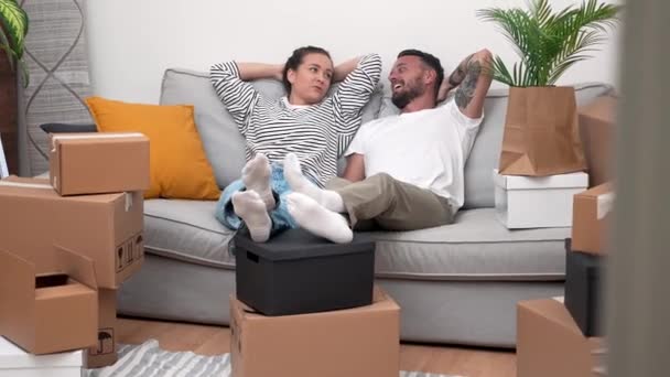 这对疲惫而又快乐的夫妇靠在沙发上 身边围着移动的纸盒 谈论着房子的装修和新公寓的装修 — 图库视频影像