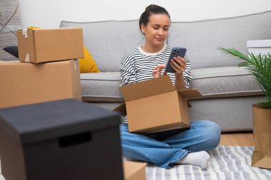 Kadın telefonda, modern evdeki kanepenin yanındaki vites kutusuyla kocasını çağdaş apartman dekorasyonuna yardım etmesi için bekliyor.