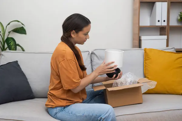Decor Devotee: A shopaholic woman joyfully inspects her fresh home decor parcel, affirming contentment through e-commerce and swift online shopping delivery.