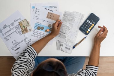 Üst görünüm belirlenmiş kadın, akıllı telefon hesap makinesi ve belgelerle desteklenen kamu hizmetleri ve banka faturalarını sayıyor. 