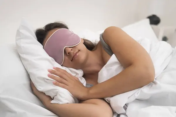 Resting female with sleep mask sleeps on light pillow covered with blanket in modern hotel apartment suite natural procedure for getting energy at night
