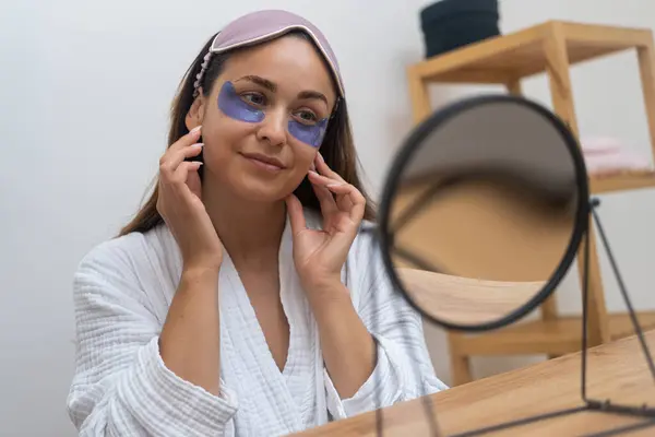 Morning Ritual A contented woman, gazing in the mirror, applies under eye masks to combat puffiness, wrinkles, and dark circles the magic of eye patches.