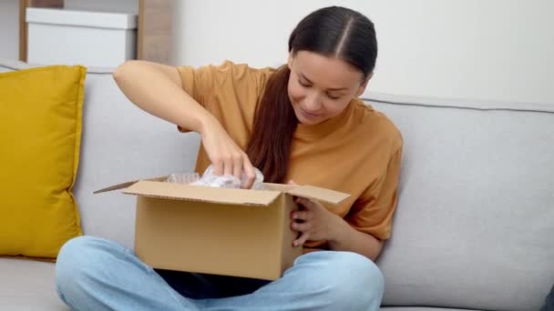 ホーム コンフォートショッピング 彼女のソファの女性は配信されたパッケージを検査し 配信で満足のいくオンラインショッピングアドベンチャーの後に喜びを表現 — ストック動画