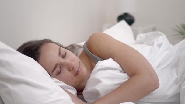 静かに眠っていた 若い女性は 明るい寝室で彼女の快適な整形外科マットレスの上に白い毛布の下に休む — ストック動画