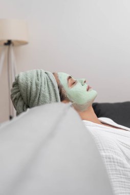 Rahatlatıcı ev spa rutininin bir parçası olarak, rahat bir kanepeye sarılıp yüz nemlendirici bir maskenin keyfini çıkarıyor.. 