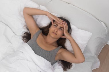  Kadın, tapınak ağrısı aşikar, nazikçe kafasına masaj yapıyor, iyi aydınlatılmış bir yatakta baş ağrısıyla savaşıyor.. 