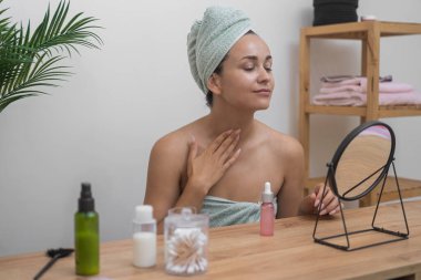 Ev spa 'sı: Havluya sarılı kadın rahatlatıcı cilt bakımını sever, aynalı masaya hyaluronik asit serumu uygular.. 