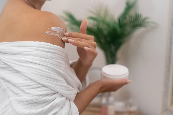 woman apply body cream from jar massages moisturizing cream onto her shoulder, personal spa.