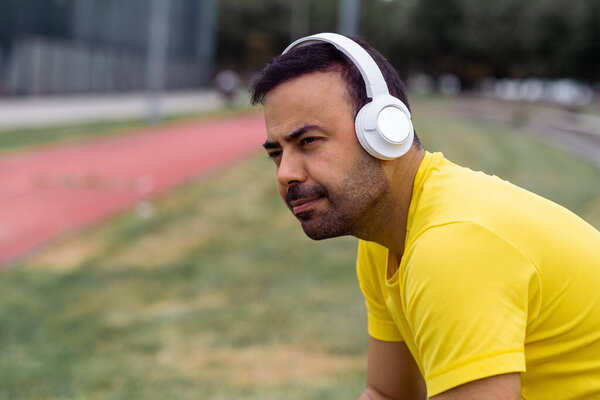 уставший спортсмен носит беспроводные наушники сидит после тренировки на спортивной арене.