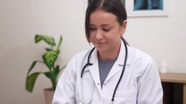 Kameraya gülümseyen kadın doktorun video portresi, çevrimiçi bir randevu sırasında hastaları sıcak bir şekilde karşılama
