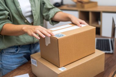 Kadınların elleri bir pakete bir QR kod etiketi yapıştırır, e-ticaret teslimatı ve çevrimiçi alışverişin özünü gösterir.. 