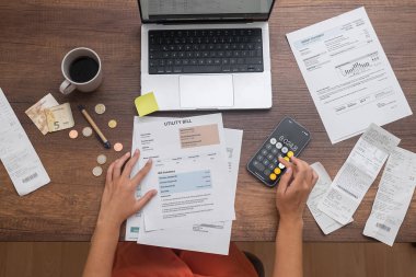 Yukarıdan, bir kadın ustalıkla mali planlama yapar, ev giderlerini hesaplar, faturaları ve parayı bir masanın üzerinde düzenler.