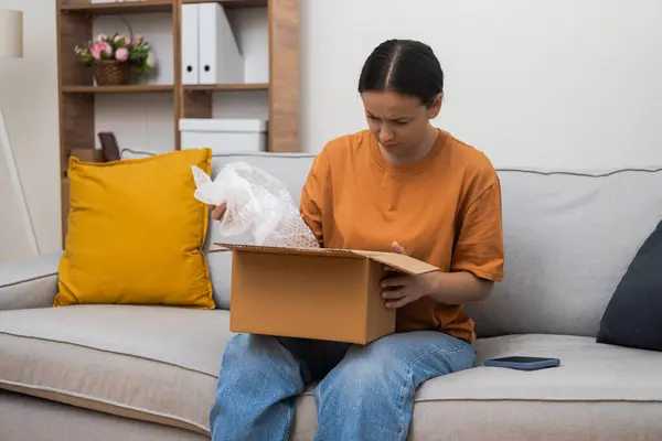 Dissatisfied woman finds defect in goods in box with filling for safety of package concept of customer dissatisfaction and purchase with home delivery