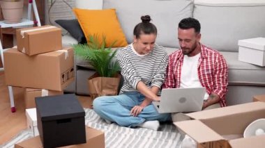 Style 'da taşınma: Taşınan kutularla çevrili genç bir çift, dizüstü bilgisayarla dekor alışverişi yapıyor, evlerini veya kitap taşıma hizmetlerini planlıyor