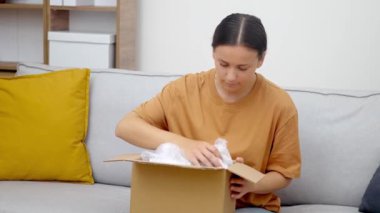 Hatalı Teslimat: Ürkmüş bir bayan yanlış teslim paketine bakıyor, hayal kırıklığı aşikar, nakliye aksiliğinden besleniyor, alt dağıtım servisine öfkeleniyor. 