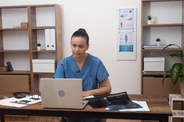 Genç doktor bilgisayardan hastaya röntgen sonuçlarından bahsediyor. Kadın tedavi planını tartışıyor ve tavsiyelerde bulunuyor.