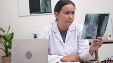 Bir hastane ortamında, bir kadın doktor ve bir radyoloji uzmanı hastaların röntgen filmlerini incelemeye odaklanırlar.