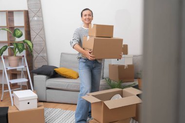 Hevesli bir kadın, elinde farklı boyutlarda karton kutularla modern bir eve taşınmaktan ve elinde kişisel eşyalarıyla bir apartman dairesinde oturmaktan mutluluk duyar.