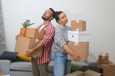 Yeni apartman sahipleri farklı boyutlarda kutular bulunduruyorlar. Tavana bakıyorlar. Genç bir ailenin taşınması ve değişmesi konusunda zorluklar var.