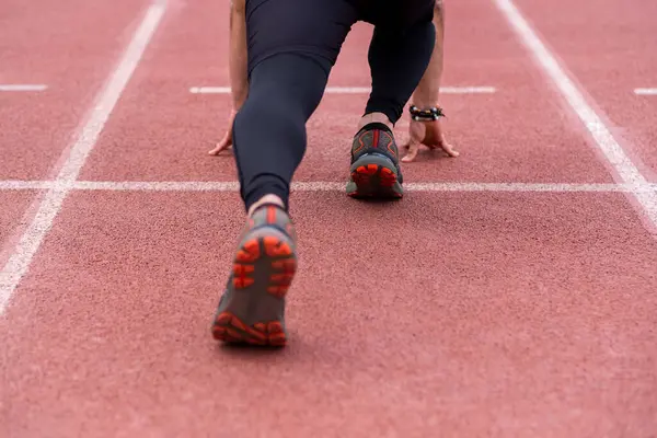 Profesyonel bir sporcunun bacaklarına odaklanmış, hareketli kırmızı kauçuk pistte koşmaya hazır, heyecan verici bir antrenmana hazır.