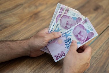 Türk lira banknotlarını elinde tutan erkek şirket muhasebecisi, döviz kurundan sonra para sayıyor ve bankadaki ahşap masada oturuyor.