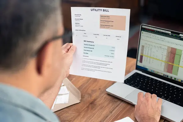 stock image Senior man holds utility bill working on computer sitting at office workplace, worried mature male person studies household expense, monthly payments organization