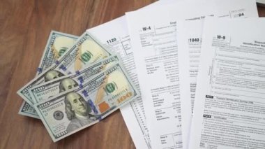 Tahta yüzeye serilmiş 100 dolarlık banknotların yanı sıra W-4 W-9 ve 1040 gibi çeşitli vergi belgelerinin finansman ile çalışma süreci