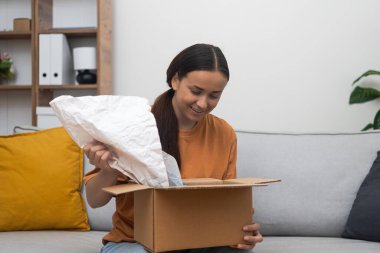 Home Delight: Kanepesinde oturan memnun bir kadın paketini açıyor, elinde bir karton kutu, online alışveriş ve teslimat sevincini somutlaştırıyor. 