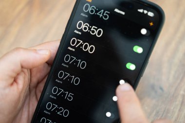 Bulanık ahşap arka planı olan bir akıllı telefon ekranında alarmı çalıştıran kişi. Verimli zaman yönetimi ve günlük programlama konsepti. Teknoloji ve üretkenlik temaları için mükemmel 