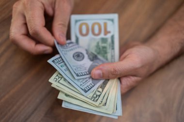 Tahta bir masadaki Amerikan dolarlarını saymak için yakın plan çekimler. Finansal işlemler ve nakit işleme konsepti. Ekonomi, bankacılık ve iş konuları için uygun 