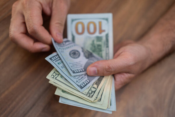 Крупным планом руки, считая долларовые купюры на деревянном столе. Финансовые операции и концепция обработки наличных денег. Подходит для тем по экономике, банковскому делу и бизнесу 