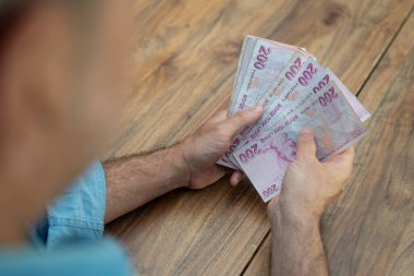 Tahta zeminde Türk lirası banknotları sayan kişi. Mali yönetim, para birimi enflasyonu ve ekonomik koşulları vurguluyor 