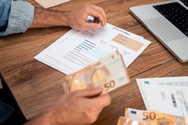 Avro banknotlarını ev giderleri için tutarken faturayı inceleyen adam. Faturaları hesaplamaya, vergileri yönetmeye ve çevrimiçi ödeme çözümlerine odaklan 