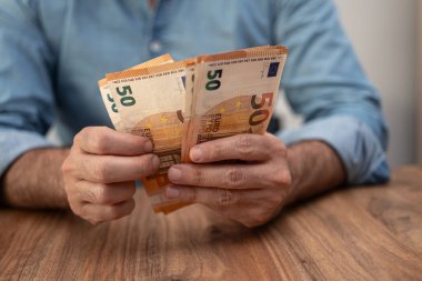 İş adamı, işyerinde oturmanın işletme giderleri kapsamında çeşitli faturaları ödemek için avro banknotlarını elinde tutuyor.