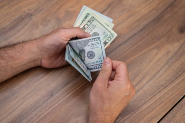Erkek girişimci, mesai bitiminden sonra masa başında oturan mevsimlik işçilere ödenmesi gereken para miktarını hazırlamak için dolar banknotlarını elinde tutuyor.