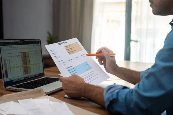 stock image Entrepreneur man with pen compares utility bill and digital sheet sitting at laptop, male employee calculates rising costs of household service filling monthly payments forms