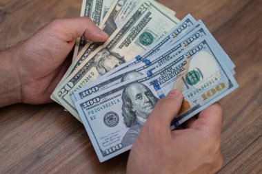 Elleri ahşap bir masada Amerikan dolarlarının çoklu değerlerini sayıyor. Finansal işlemler ve nakit yönetimi kavramı. Bankacılık, finans ve yatırım temaları için ideal 