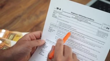 Erkek muhasebeci, W-4 çalışanını yakından inceliyor. Ağır çekimin eksiksiz tamamlandığından emin olmak için belli bir bölümü kalemle gösteren sertifika vergi belgesini saklıyor.