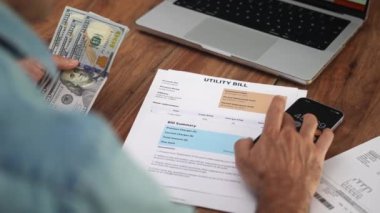 Olgun girişimci dolarları elinde tutuyor, toplam telefon miktarını hesaplıyor, iş adamı faturaları ağır çekimde ödemek için toplamı belirleyen hesaplamalar yapıyor.