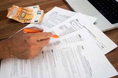 Girişimci, işyerinde avro banknotları ve dizüstü bilgisayarla oturan işletme sahipleri için zorunlu olan karmaşık vergi formlarını dolduran evrak işleriyle uğraşıyor