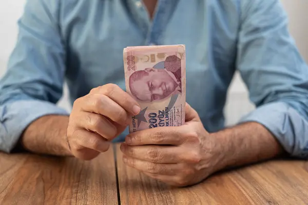 stock image Man holding a stack of Turkish lira banknotes on a wooden table. Economic concept illustrating inflation and finance in Turkey. 